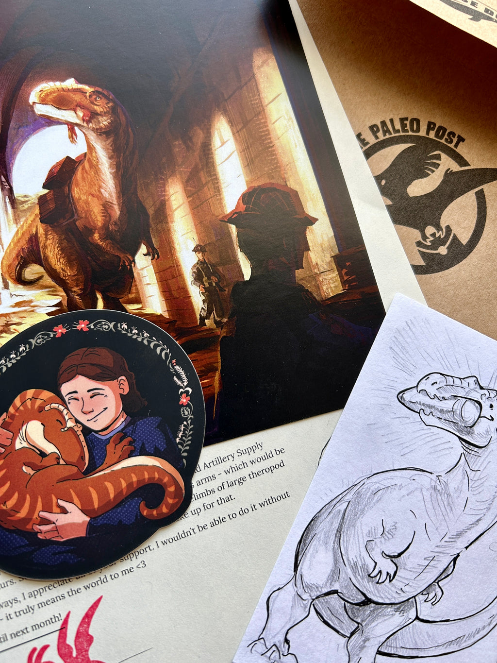 Collection of dinosaur-themed items including a sticker, illustration, and card on top of a letter describing the history behind the illustrations created. 