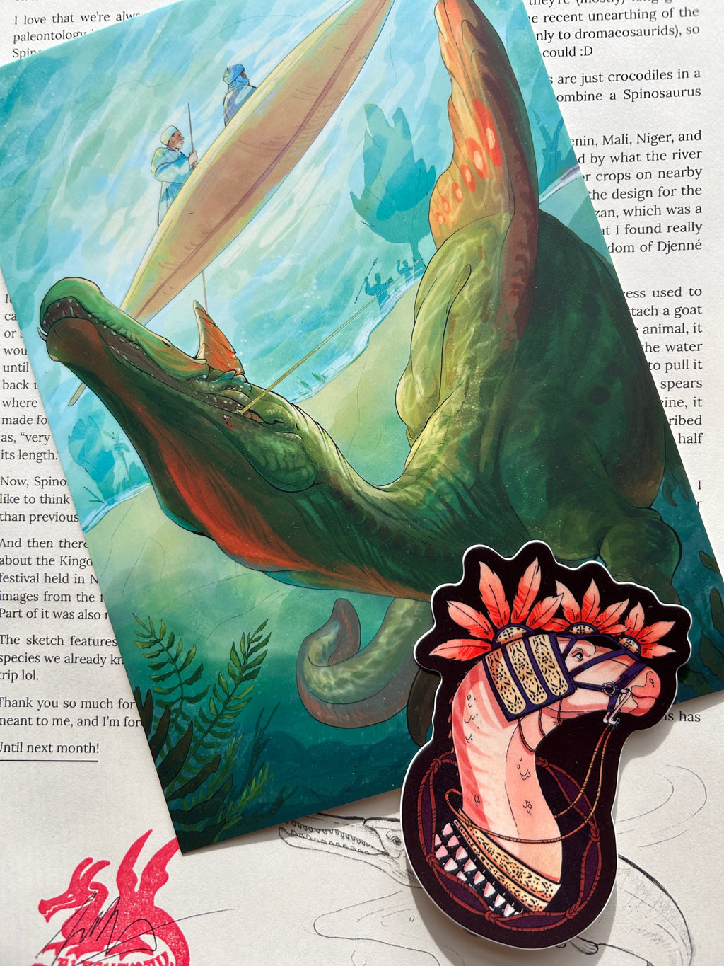 Picture of the print, sticker, and letter that comes with the April edition of The Paleo Post. A Spinosaurus Mirabilis and a Lurdusaurus are both featured. 