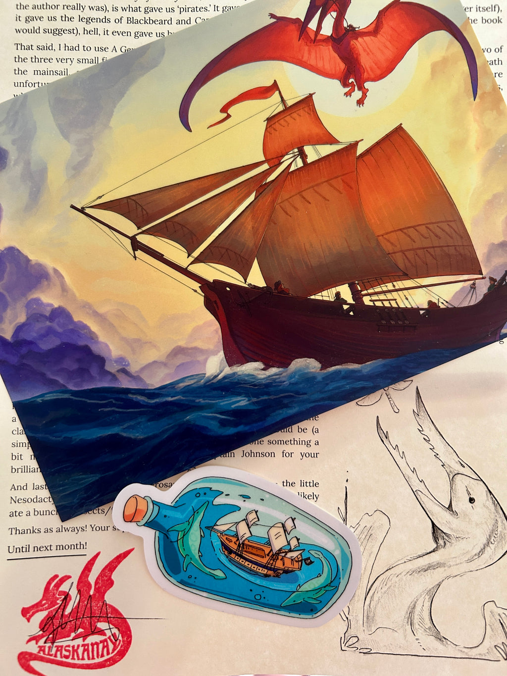A hatzegopteryx flying above a pirate sloop on a 5x7 print, a letter, and a sticker featuring a ship in a bottle
